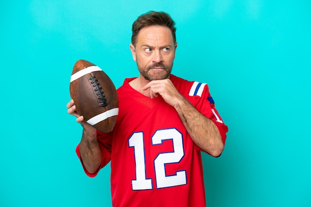 Middle age caucasian man playing rugby isolated on blue background having doubts and thinking