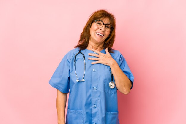 Middle age caucasian nurse woman isolated laughs out loudly keeping hand on chest.