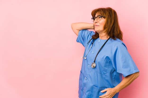 Middle age caucasian nurse woman isolated touching back of head, thinking and making a choice.