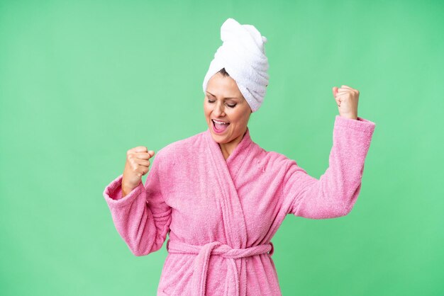 Middle age caucasian woman in a bathrobe over isolated background celebrating a victory