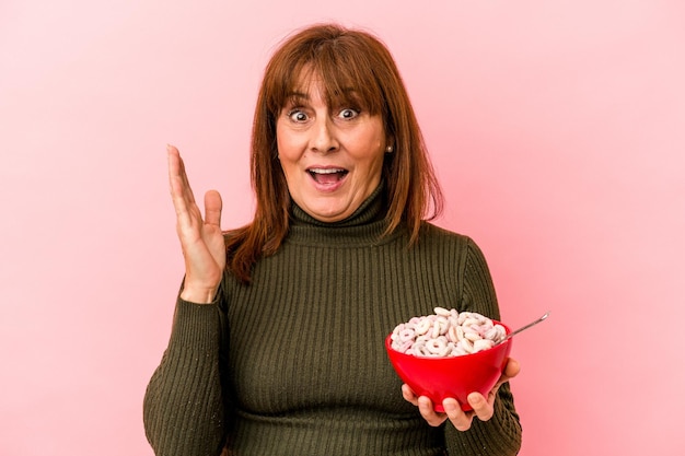 Middle age caucasian woman holding bowl of cereals isolated on pink background surprised and shocked.