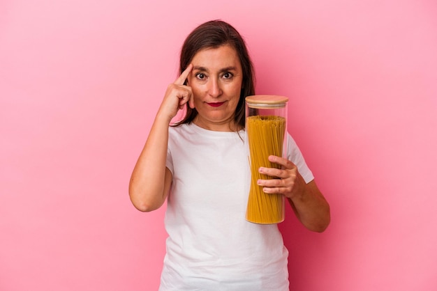 Middle age caucasian woman holding a pasta jar isolated on pink background pointing temple with finger, thinking, focused on a task.
