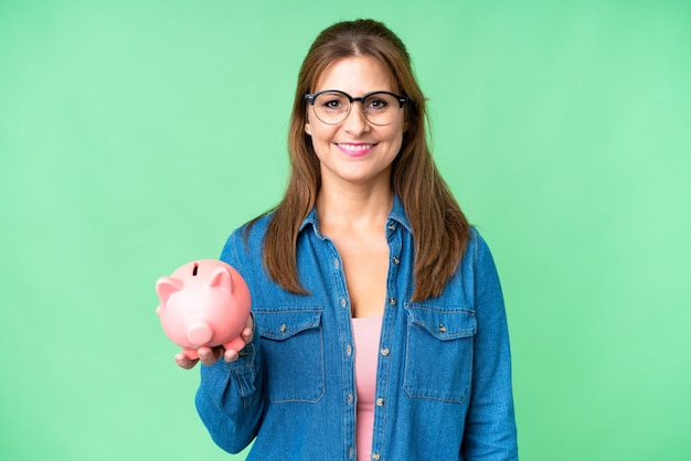 孤立した背景の上に貯金箱を保持している中年の白人女性がたくさん笑っている