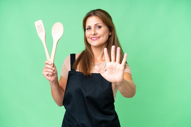 Middle age caucasian woman holding a rolling pin over isolated background counting five with fingers