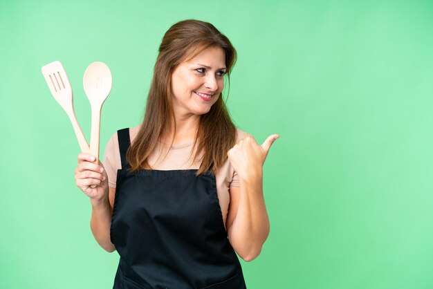 Middle age caucasian woman holding a rolling pin over isolated background pointing to the side to present a product