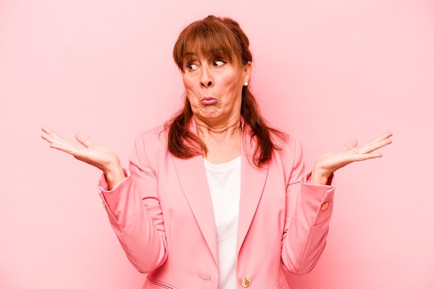 Middle age caucasian woman isolated on pink background confused and doubtful shrugging shoulders to hold a copy space