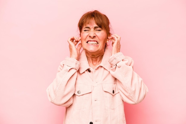 Photo middle age caucasian woman isolated on pink background covering ears with hands