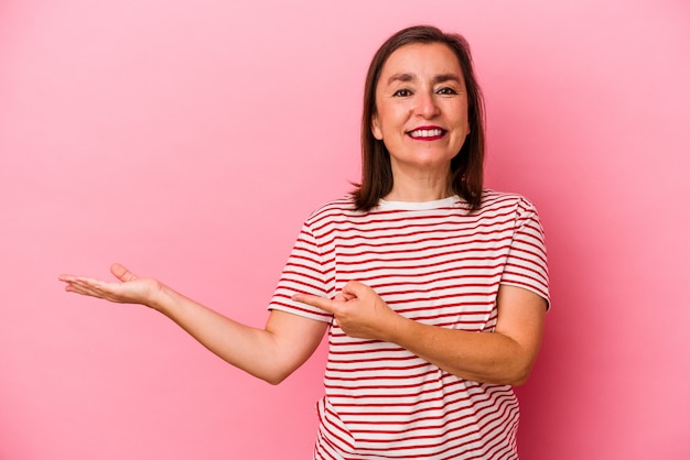 Middle age caucasian woman isolated on pink background excited holding a copy space on palm.