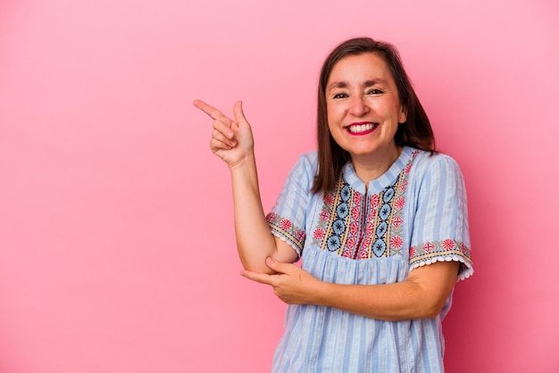 Middle age caucasian woman isolated on pink background pointing with forefingers to a copy space, expressing excitement and desire.