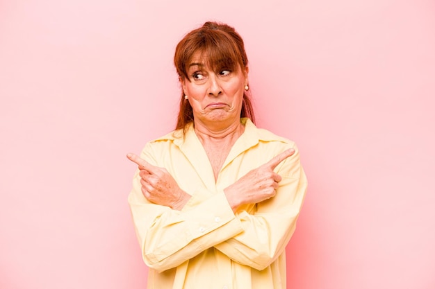 Middle age caucasian woman isolated on pink background points sideways is trying to choose between two options