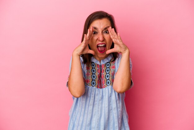 Middle age caucasian woman isolated on pink background shouting excited to front.