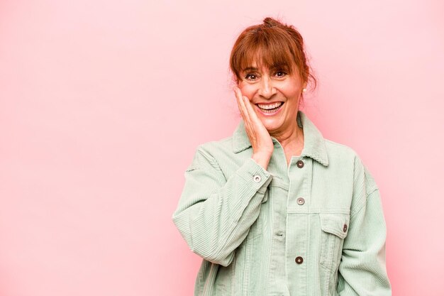 Middle age caucasian woman isolated on pink background shouts loud keeps eyes opened and hands tense