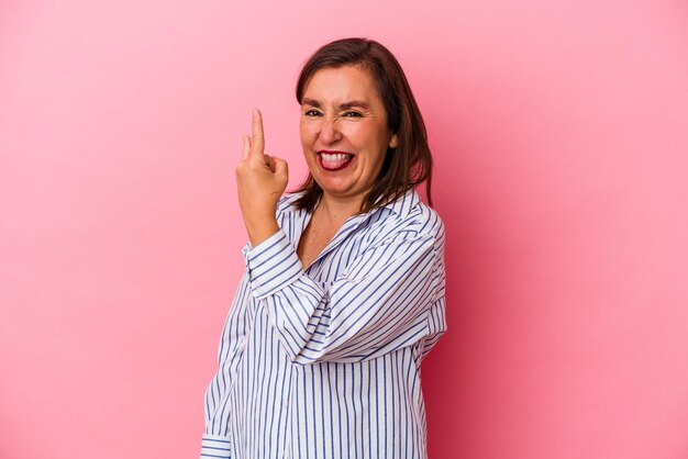 Middle age caucasian woman isolated on pink background showing rock gesture with fingers