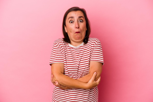 Middle age caucasian woman isolated on pink background shrugs shoulders and open eyes confused.