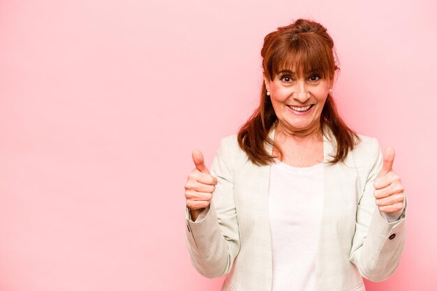 Middle age caucasian woman isolated on pink background smiling and raising thumb up