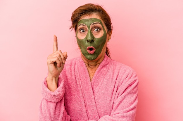 Middle age caucasian woman wearing a facial mask isolated on pink background having some great idea, concept of creativity.