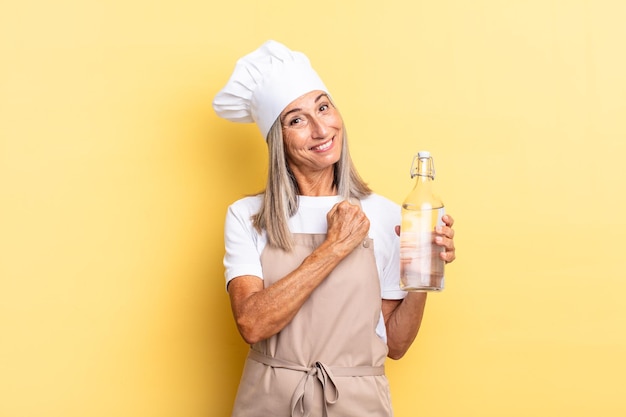 Middle age chef woman feeling happy positive and successful motivated when facing a challenge or celebrating good results with a water bottle