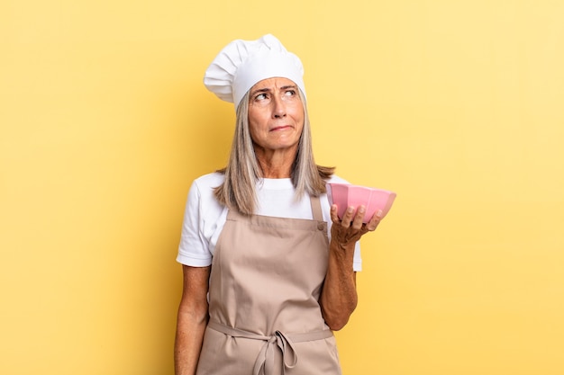 Middle age chef woman feeling sad, upset or angry and looking to the side with a negative attitude, frowning in disagreement and holding an empty pot