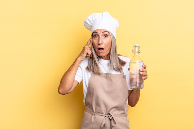 Middle age chef woman looking surprised openmouthed shocked realizing a new thought idea or concept with a water bottle