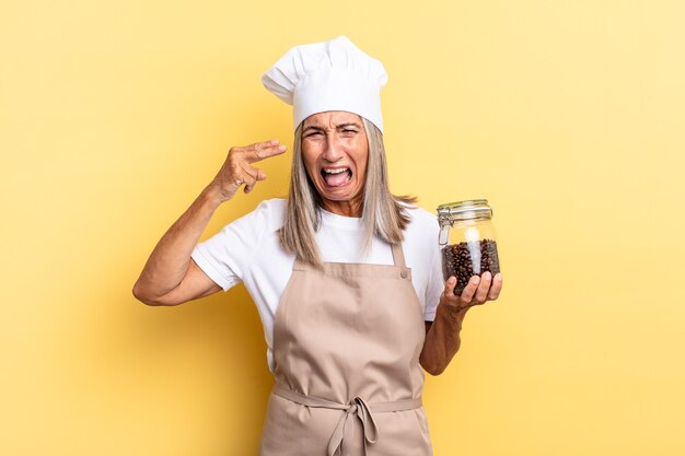 Middle age chef woman looking unhappy and stressed, suicide gesture making gun sign with hand, pointing to head holding coffee beans