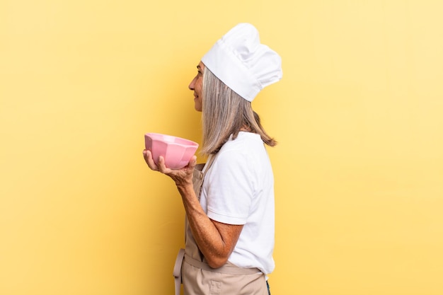 Donna chef di mezza età in vista di profilo che cerca di copiare lo spazio avanti, pensando, immaginando o sognando ad occhi aperti e tenendo in mano un vaso vuoto