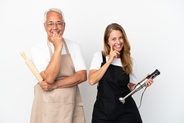 Middle age chefs couple isolated on white background smiling with a sweet expression