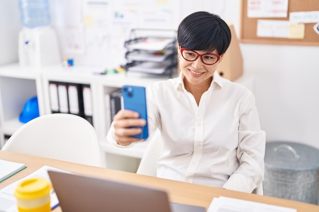 中年中国人女性ビジネス ワーカーがオフィスでスマート フォンで selfie を作る