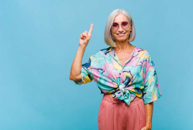 Middle age cool woman smiling cheerfully and happily, pointing upwards with one hand to copy space