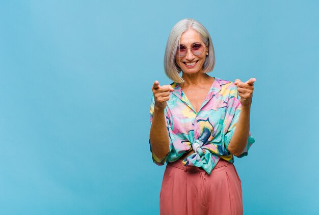 Middle age cool woman smiling with a positive, successful, happy attitude pointing to the camera, making gun sign with hands