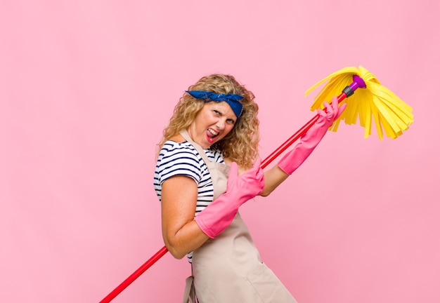 Middle age cool woman with a mop against pink wall