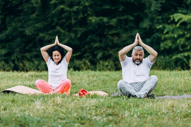 Middle age couple  doing yoga together outdoors making gesture namaste under they heads.   