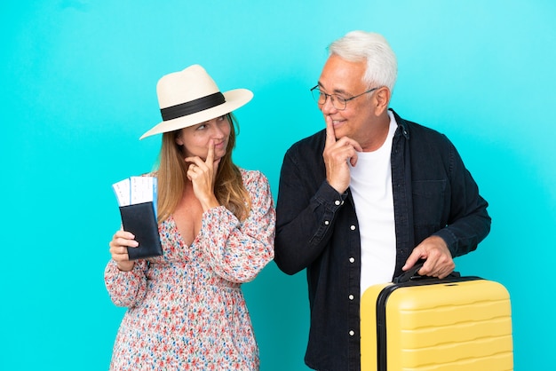 Middle age couple going to travel and holding a suitcase isolated on blue background looking looking at each other