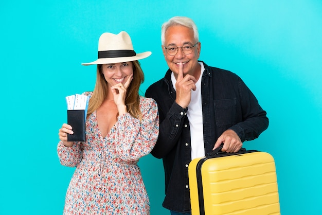 Пара среднего возраста собирается в путешествие и держит чемодан на синем фоне, улыбаясь со сладким выражением лица