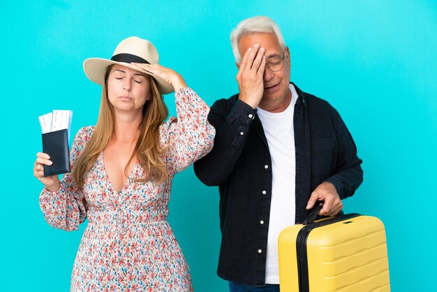 Middle age couple going to travel and holding a suitcase isolated on blue background with surprise and shocked facial expression