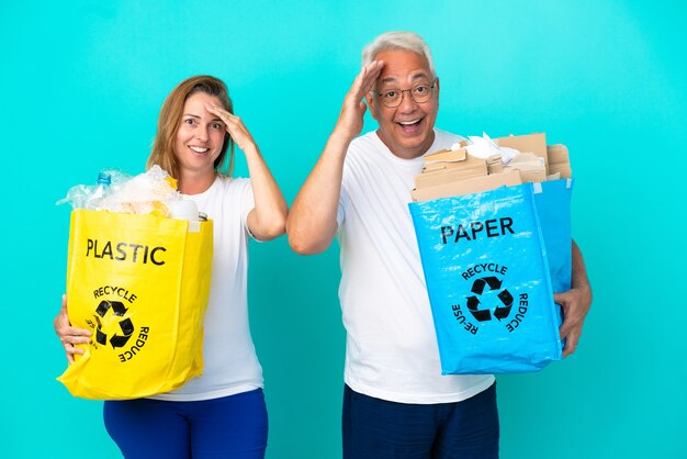 白い背景で隔離の紙とプラスチックでいっぱいのリサイクルバッグを保持している中年夫婦はちょうど何かを実現し、解決策を意図しています