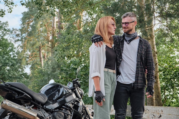 Middle age couple hugging and having fun on a motorcycle traveling together on a forest road