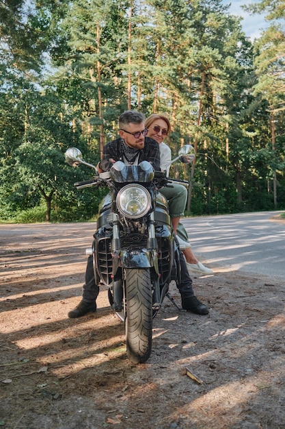 Middle age couple hugging and having fun sitting on a\
motorcycle traveling together on a forest road