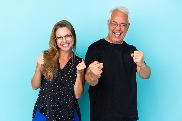 Middle age couple isolated on blue background celebrating a victory