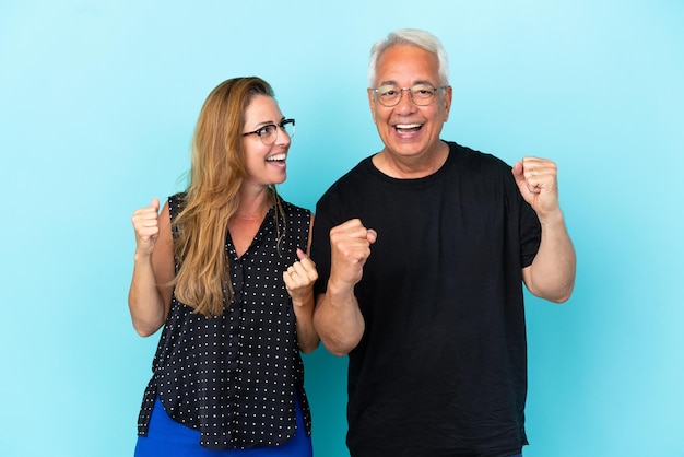 Middle age couple isolated on blue background celebrating a victory