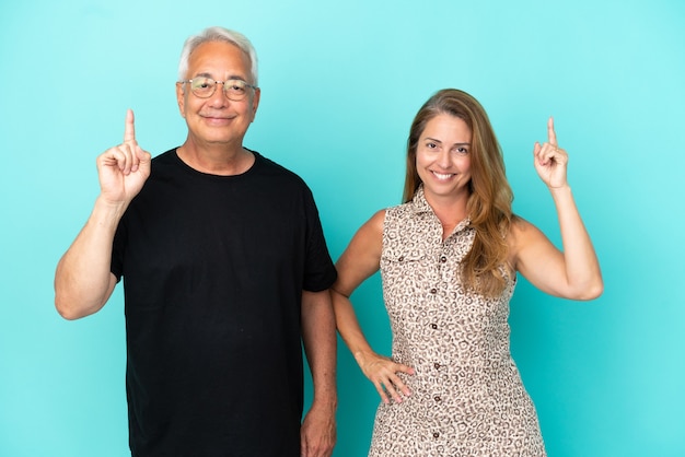 Middle age couple isolated on blue background showing and lifting a finger in sign of the best