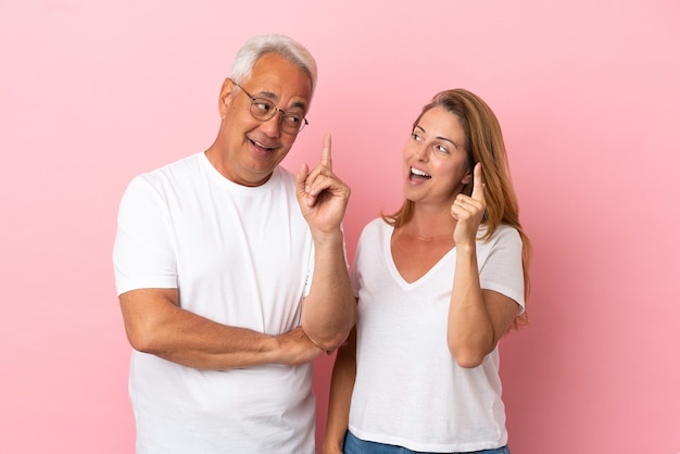 Middle age couple isolated on pink background intending to realizes the solution while lifting a finger up