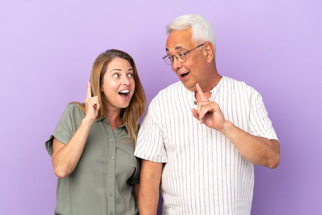 Middle age couple isolated on purple background intending to realizes the solution while lifting a finger up