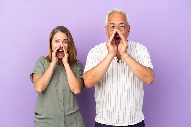 Middle age couple isolated on purple background shouting and announcing something