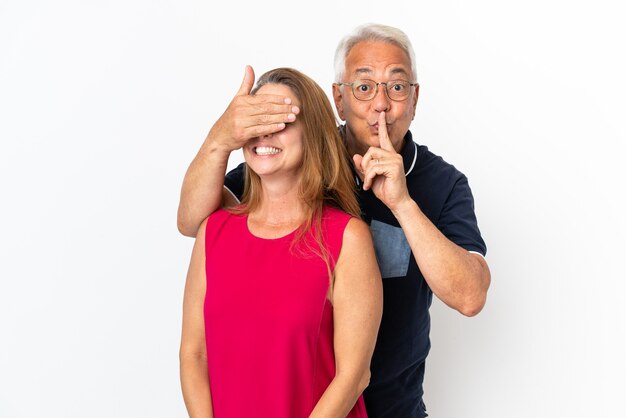 Middle age couple isolated on white background covering her eyes to surprise her