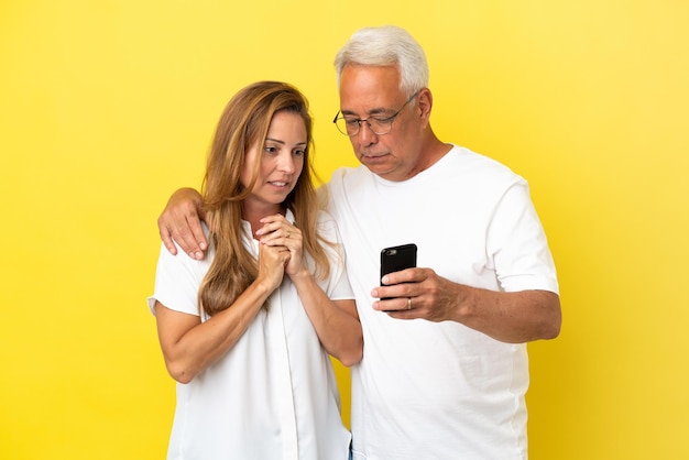 Coppia di mezza età isolata su sfondo giallo leggendo un messaggio con il cellulare