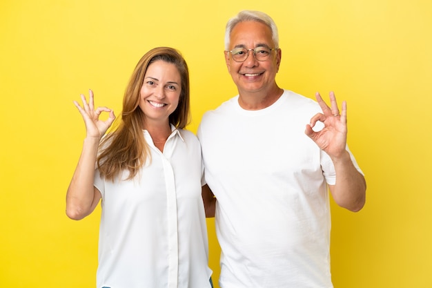 Пара среднего возраста, изолированные на желтом фоне, показывая пальцами знак ОК