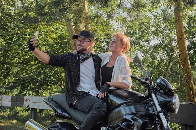 Middle age couple riding a motorcycle having fun and taking a selfie on a mobile phone camera