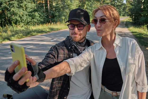 Coppia di mezza età in sella a una motocicletta divertendosi e facendo un selfie con la fotocamera di un cellulare