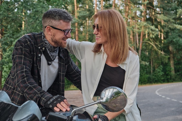 Middle age couple talking and having fun sitting on a motorcycle traveling together on a forest road