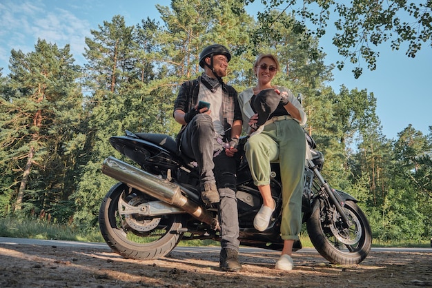 Middle age couple talking and having fun sitting on a motorcycle traveling together on a forest road